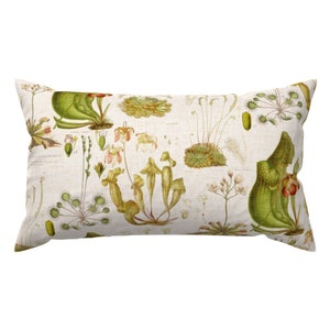 Puede incluir: Una almohada rectangular con un fondo de lino blanco que presenta una ilustración botánica de varias plantas carnívoras en tonos verdes, marrones y rosas.