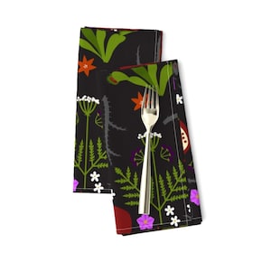 Peut inclure: Deux serviettes en tissu noir avec un motif floral. Le motif présente des feuilles vertes, des fleurs rouges et orange, et des fleurs violettes et blanches. Les serviettes sont pliées en deux et placées sur un fond blanc.