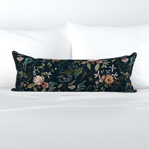 May include: A long, rectangular lumbar pillow featuring a dark navy blue background with a dense, multi-colored botanical print. The pattern includes various flowers, leaves, and stems in shades of cream, peach, sage green, and muted brown.