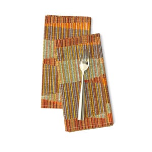 May include: Two orange, yellow, and brown striped fabric napkins folded together with a silver fork on top.