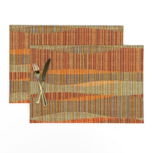 May include: Two orange, brown, and green striped placemats with a woven texture. The placemats are made of fabric and have a subtle wave pattern.