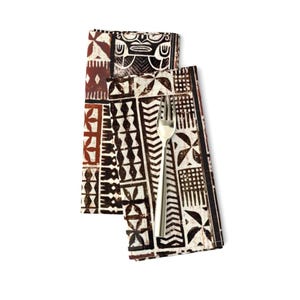 May include: Two brown and white patterned fabric napkins with a silver fork on top. The pattern is a geometric design with a repeating motif of a tiki mask.