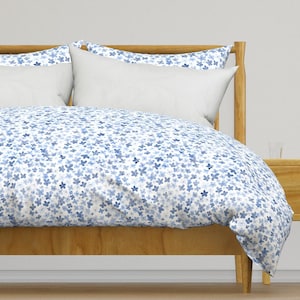 May include: A white duvet cover with a blue floral pattern. The duvet cover is on a wooden bed frame with a white pillow and a blue floral patterned pillow.