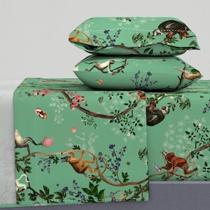 May include: Bed linen set with a jungle-themed design. The teal sheets and pillowcases display a repeating pattern of monkeys, sloths, and butterflies amongst flowering branches. The design includes shades of brown, pink, and blue.