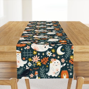 Op de afbeelding: Een teal tafelkleed met een herhalend patroon van witte geesten, oranje pompoenen en bloemen. De geesten dragen bloemenkransen en glimlachen. De tafelkleed is perfect voor een Halloween-feest of diner.
