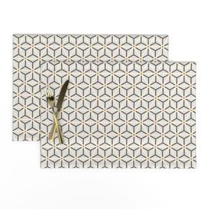 May include: Two beige placemats with a geometric pattern of black lines and small gold circles. The placemats are stacked on top of each other.