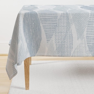 May include: A white tablecloth with a blue and white geometric pattern. The tablecloth is draped over a table with wooden legs.