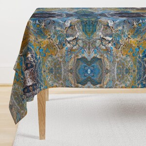 May include: A blue, brown, and gold abstract tablecloth with a symmetrical pattern. The tablecloth is made of a soft, durable fabric and is perfect for adding a touch of modern style to any dining room.