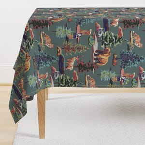 May include: A green tablecloth with a repeating pattern of colorful woodland animals and trees. The animals include a bear, deer, wolf, and birds. The trees are a mix of pine and deciduous trees.