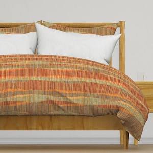 May include: A brown, orange, and green striped duvet cover with a white pillow on a wooden bed frame.