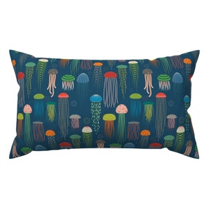 Op de afbeelding: Een marineblauw kussen met een herhalend patroon van kleurrijke kwallen. De kwallen zijn in verschillende tinten roze, oranje, geel, groen, blauw en paars. De achtergrond is donkerblauw.