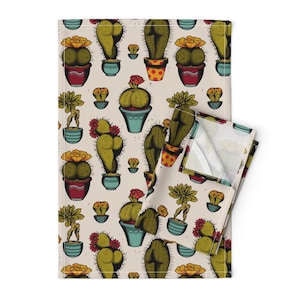 May include: A kitchen towel with a repeating pattern of cacti in various colors and styles. The cacti are in pots and some have flowers. The background is a light beige color.