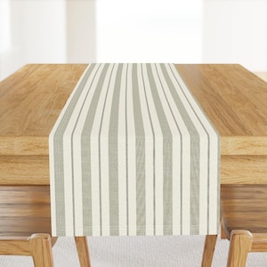 May include: A white and gray striped table runner. The runner is made of a woven fabric and has a subtle texture.
