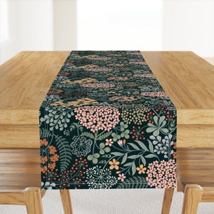 May include: A dark green table runner with a floral pattern featuring pink, yellow, and orange flowers. The runner has a white border and is made of a soft, durable fabric.