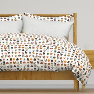 May include: White duvet cover with a repeating pattern of colorful dog faces. The duvet cover is on a wooden bed frame with two white pillowcases.