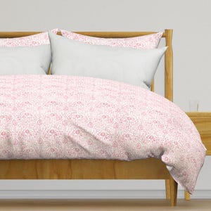 Op de afbeelding: Een wit en roze bloemenpatroon dekbedovertrek op een houten bedframe. Het dekbedovertrek heeft een delicaat bloemenpatroon in roze tinten.