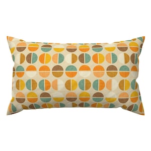 May include: A rectangular throw pillow with a beige background and a repeating pattern of colorful circles. The circles are divided in half, with one half being a solid color and the other half being a different solid color. The colors used are orange, yellow, brown, and teal.