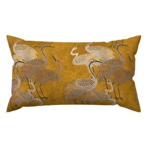 Pode incluir: Uma almofada retangular com fundo amarelo mostarda e um padrão repetitivo de grous cinzentos e brancos. As aves estão representadas em várias poses com texturas de penas detalhadas, pescoços longos e pernas finas na superfície.