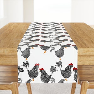 May include: White table runner with a repeating pattern of black and white chickens with red combs. The chickens are facing different directions and some are standing while others are walking.