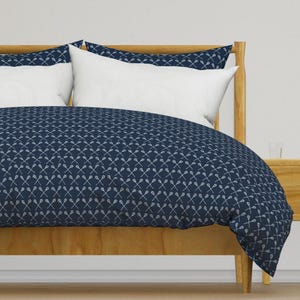 Könnte beinhalten: Ein dunkelblauer Bettbezug mit einem weißen Lacrosse-Schläger-Muster. Der Bettbezug liegt auf einem Bett mit einem Holz-Kopfteil und zwei weißen Kissen.