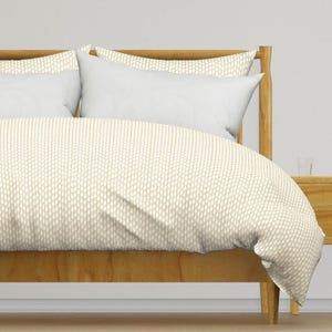 May include: A beige duvet cover with a subtle white pattern, shown on a bed with a wooden headboard and white pillows.