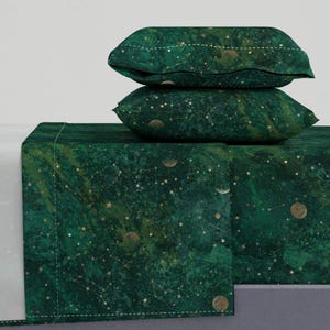 May include: A green and gold bedding set with a celestial print featuring stars, moons, and constellations. The set includes a flat sheet, fitted sheet, and two pillowcases.