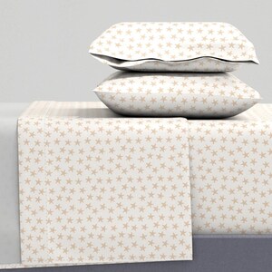 May include: A bedding set featuring a cream-colored background with a repeating pattern of tan starfish. The set includes two pillowcases and a fitted sheet. The pillowcases are stacked on top of the fitted sheet, creating a layered effect.