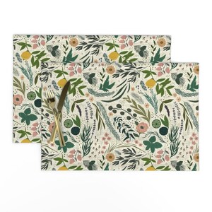 May include: A set of two placemats featuring a floral pattern with a cream background. The pattern includes green leaves, pink flowers, yellow lemons, and other botanical elements.