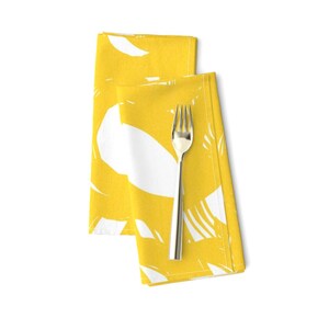 May include: Two yellow napkins with a white abstract design. The napkins are folded and a silver fork is placed on top.