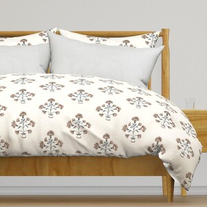 May include: A white duvet cover with a floral pattern in shades of brown and blue. The duvet cover is on a bed with a wooden headboard and a white pillow.
