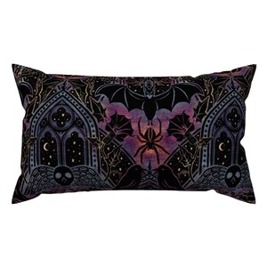 Puede incluir: Una almohada decorativa negra y dorada con un arco gótico, murciélagos, arañas y estrellas sobre un fondo degradado morado y rosa.