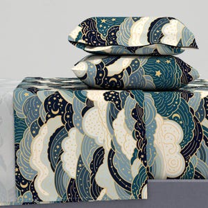 Pode incluir: Um conjunto de roupa de cama azul e branco com um padrão de nuvens e estrelas. O conjunto inclui um lençol de cima, um lençol de baixo e duas fronhas.