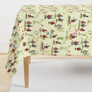 May include: A light yellow tablecloth featuring a repeating pattern of anthropomorphic ladybugs engaged in various activities, including walking with canes, playing musical instruments, and holding umbrellas, interspersed with small colorful flowers.