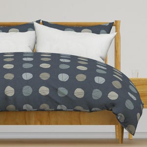 May include: A blue duvet cover with a white and gray polka dot pattern. The duvet cover is on a bed with a wooden headboard and a white pillow.