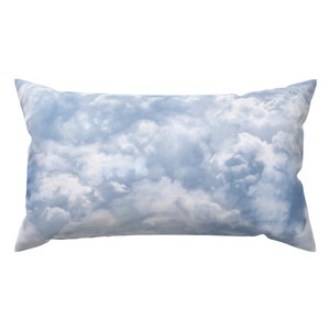 May include: A rectangular pillow with a cloud design. The pillow features a light blue background with white fluffy clouds, creating a soft and airy aesthetic. The pillow is designed for decorative use.