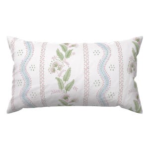 Puede incluir: Una almohada rectangular blanca con un estampado floral. El diseño presenta rayas verticales con patrones alternos de elementos florales y punteados rosas, celeste y verdes. La almohada está diseñada para uso decorativo.