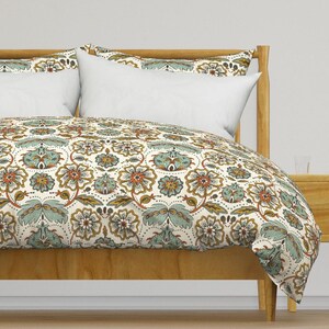 May include: A white duvet cover with a floral pattern in shades of teal, orange, and gold. The duvet cover is on a wooden bed frame.