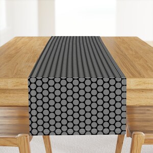 May include: A black and gray table runner with a repeating pattern of gray circles. The runner is on a wooden table.
