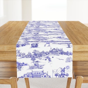 May include: Blue and white table runner with a repeating pattern of a golf course scene. The design includes a golf course, houses, trees, and people playing golf.