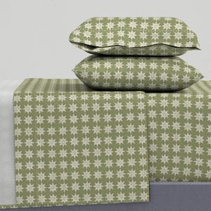 May include: A bedding set featuring two rectangular pillows stacked on top of a flat sheet, all decorated with a repeating pattern of white eight-pointed stars on a muted olive green background, creating a consistent and uniform visual design.