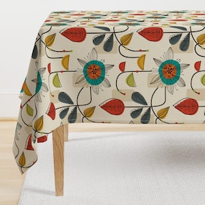 May include: A beige tablecloth with a retro floral pattern. The pattern features stylised flowers in shades of teal, orange, red, and yellow, with leaves in shades of green, red, and grey. The tablecloth is shown draped over a table with wooden legs.