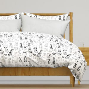 Puede incluir: Una funda nórdica blanca con estampado de perros en blanco y negro. La funda nórdica está en una cama con cabecero y marco de madera.