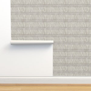 Puede incluir: Un rollo de papel tapiz con un patrón geométrico blanco y gris. El papel tapiz está parcialmente desenrollado y está colgado en una pared blanca.