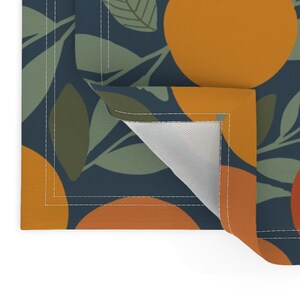May include: A close-up of a blue placemat with a repeating pattern of orange circles and green leaves. The placemat is folded to show the white underside.