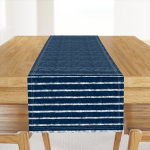 May include: A blue and white striped table runner with a distressed look. The runner is made of fabric and has a white border.