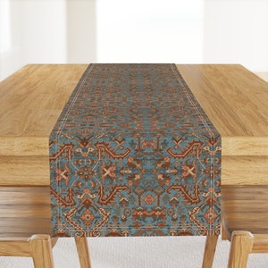 May include: A blue and brown patterned table runner with a geometric design. The runner has a white border and is made of a soft, woven fabric.