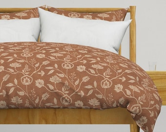 May include: A brown duvet cover with a white floral pattern. The duvet cover is on a bed with a wooden headboard and two white pillows.