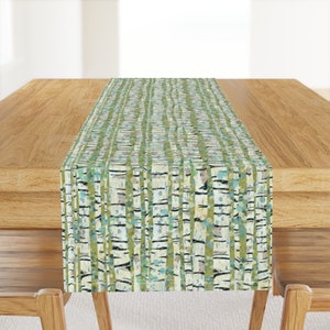 Op de afbeelding: Een groene en witte tafelrunner met een berkenboompatroon. De runner ligt op een houten tafel.