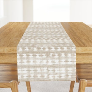 May include: A beige table runner with a white geometric pattern. The runner is on a wooden table.