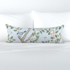 May include: A light blue lumbar pillow with a floral pattern featuring a bird, branches, and flowers. The pillow has a white background with a subtle blue tint.
